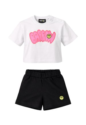 T-shirt bianca corta con scritta rosa "Barrow" e toppa smiley, abbinata a pantaloncini con vita elastica neri con una piccola toppa smiley.