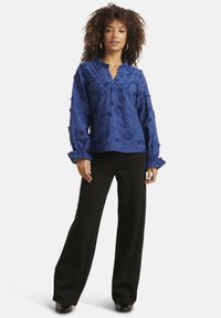 Blue floral blouse with long sleeves, ruffled neckline, and cuffs, paired with black wide-leg trousers and round-toe shoes.