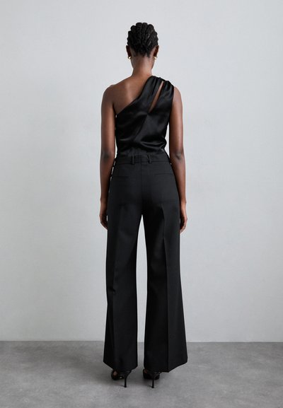 Sort satin top med én skulderstrop og et nøglehul detaljer, parret med højtaljede sorte vidde bukser, der fremhæver en skræddersyet pasform.