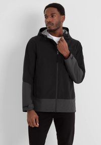 Black waterproof jacket with a grey hood and accents, textured fabric, zip closure, and adjustable cuffs. Minimalistic design, practical fit.