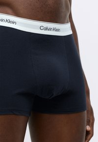 Navy cotton boxer shorts with a white waistband featuring "Calvin Klein" logo in black. Smooth texture, fitted design.