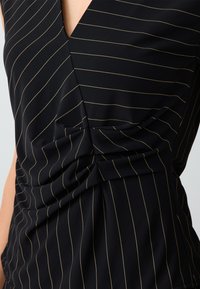 Top nero con strisce verticali dorate, scollatura a V profonda e tessuto arricciato di lato, realizzato in materiale leggero.