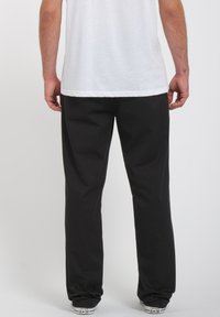 Pantalones negros con diseño de pierna recta. Fabricados con un tejido suave, cuentan con una cinturilla elástica y puños. Se llevan con una camiseta blanca y zapatillas.