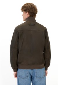 Brun læderjakke med høj krave, som har en glat overflade og ribbede manchetter, parret med lyseblå denimbukser.