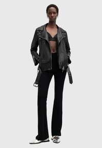 Black leather biker jacket with silver stud embellishments, zip pockets, and belted waist, paired with a black top and flared pants.
