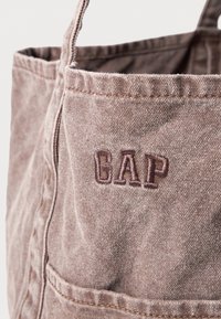 Braune Canvas-Shopper-Tasche mit strukturiertem Finish, versehen mit einem gestickten "GAP"-Logo und zwei stabilen Tragegriffen. Mit einem vorderen Taschen-Detail.