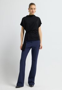 Top corto negro de manga corta con detalle de frente retorcido, combinado con pantalones acampanados azul marino y zapatos negros de punta. Textura de tela suave.