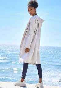 Cárdigan con capucha de color gris claro, de corte oversized, material suave, superpuesto sobre leggins azul marino con detalles de botones y combinado con zapatillas blancas.
