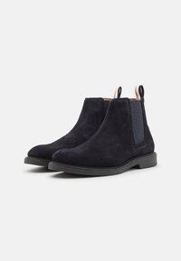 Bottes chelsea en suède navy avec des panneaux latéraux élastiques, des accents texturés, des semelles en caoutchouc noires et des languettes pour un enfilage facile.