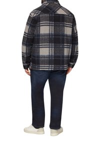Kariertes Flanelljackett in Beige, Marineblau und Schwarz, mit kragenförmigem Hals und Knopfmanschetten, getragen über dunklen Jeans und weißen Sneakers.