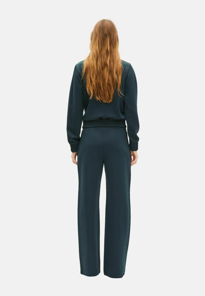 Donkergroene sweatshirt en bijpassende wijde broek set. Zachte stof, ribbelmanchetten en tailleband. Ontspannen pasvorm, minimale details en strakke lijnen.
