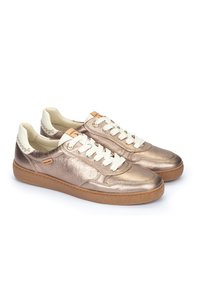 Zapatillas metálicas en color rosa dorado con cordones blancos, suelas de goma color beige y sutiles dibujos en el talón y la lengua. Textura de cuero suave.