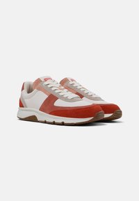 Sportowe sneakersy o mieszanej konstrukcji materiałowej, z białą skórą, czerwonymi zamszowymi akcentami i jasnoróżowym materiałem na języku.