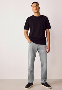 Tricou negru din bumbac, blugi gri din denim și pantofi sport negri. Ținuta are o croială lejeră, design minimalist și textură subtilă în țesătură.