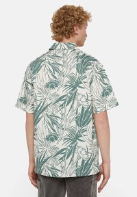 Camicia a maniche corte con un motivo floreale verde e bianco su uno sfondo chiaro, realizzata in morbido cotone leggero.
