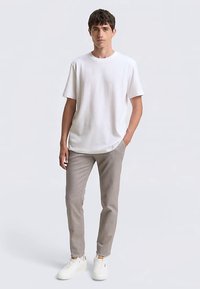 Wit t-shirt met korte mouwen, gecombineerd met lichtgrijze slim-fit broek en witte sneakers, met een comfortabele pasvorm en een gladde textuur.
