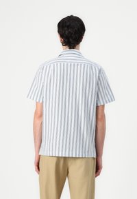 Camisa de manga corta en azul claro con rayas verticales oscuras, que presenta un cuello clásico y una parte trasera de corte recto.