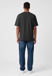 T-shirt grigio scuro a maniche corte, scollatura rotonda e vestibilità ampia, abbinato a jeans di denim blu con gamba dritta e tasche posteriori.