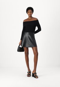 Top nero scollato abbinato a una mini gonna in pelle nera. Gli accessori includono una piccola borsa nera e sandali con tacco neri.