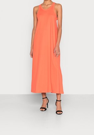 Femme portant une robe longue sans manches de couleur corail avec un col en U et des sandales à talons noirs sur un fond uni.