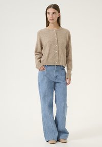 Beige Wolle-Mix Cardigan mit rundem Hals und Knopfverschluss, kombiniert mit hellblauen, vertikal gestreiften, weiten Hosen.