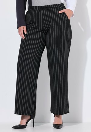 Pantaloni a gamba larga a righe bianche e nere con fondo a risvolto, dotati di vita piatta e tasche laterali, abbinati a tacchi alti neri.