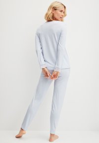 Lichtblauw pyjama set bestaande uit een lang mouwtop met kantafwerking aan de mouwen en bijpassende strakke broek. Zachte stof en relaxte pasvorm.
