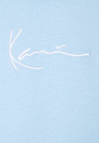 Ljust blått tyg med en mjuk textur har vit broderad text som liknar en signatur. Designen är enkel utan några ytterligare mönster.