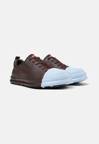Brown leather sneakers with a light blue rubber toe cap, featuring laces, a textured sole, and red branding on the tongue.