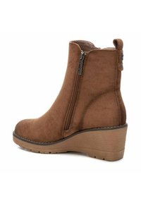 Stivaletti alla caviglia in suede marrone con cerniera laterale e tacco a zeppa. Caratterizzati da una texture liscia e una punta rotonda, offrono una silhouette moderna.