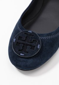 Ballerines en suede navy avec accent logo rond, coutures décoratives en violet, bout arrondi et doublure intérieure douce.