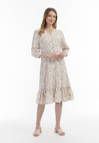 Blumen-Midi-Kleid mit V-Ausschnitt und dreiviertellangen Ärmeln, aus leichtem Stoff gefertigt, mit volanartigem Saum. Die Farben umfassen Creme, Rot und Grün.