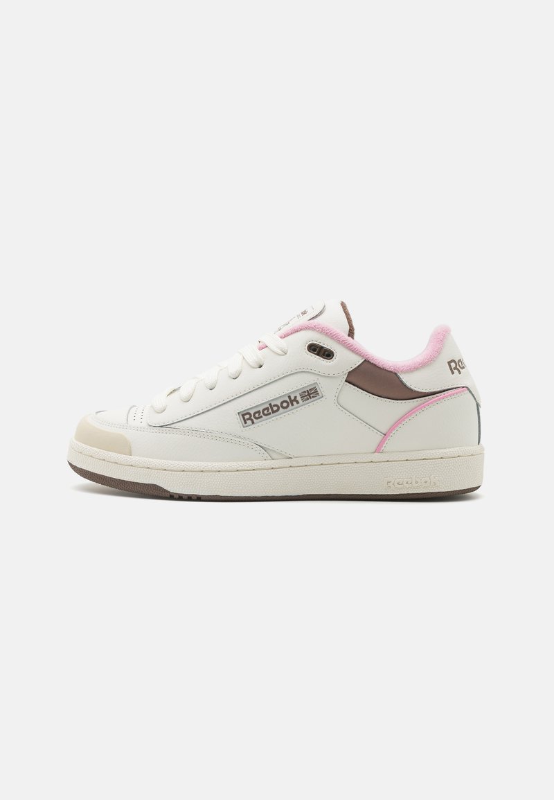 Sneaker in pelle bianca con accenti rosa e marrone, punta rotonda, design classico con lacci e suola in gomma testurizzata. Logo Reebok sul lato.