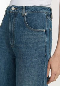 Hoge taille blauwe denim jeans met een recht model, voorzien van voorzakken, koperen stiksels en een metalen knoopsluiting.