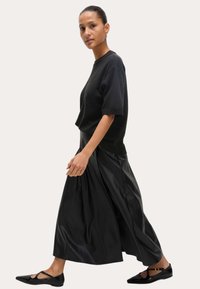 Haut à manches courtes noir en tricot associé à une jupe fluide en cuir noir et des chaussures plates noires. Texture lisse, jupe longue jusqu'à la cheville avec des plis.