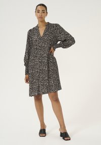 Robe à manches longues en imprimé animal noir et beige, avec un décolleté en V profond et des poignets élastiques froncés. Modèle associé à des sandales à glissière noires.