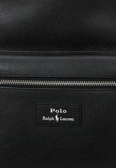 Primo piano di una borsa in pelle nera testurizzata con cerniera argentata e toppa con il logo Polo Ralph Lauren raffigurante un cavallo e un cavaliere in bianco.