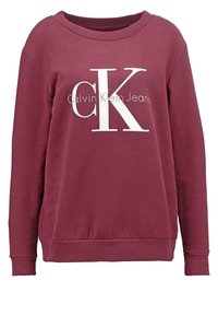 Sudadera de algodón burdeos con cuello redondo y mangas largas. Presenta un gran logo blanco "CK" y el texto "Calvin Klein Jeans". Textura suave.