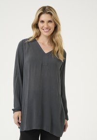 Tunic grigia a maniche lunghe con scollo a V, texture a coste e orlo asimmetrico. Il materiale sembra morbido e leggero.