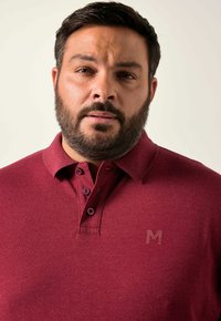 Bordeaux polo shirt met een gestructureerde stof, drie knopen en een subtiele logo op de borst. Standaard kraag en een ontspannen pasvorm.