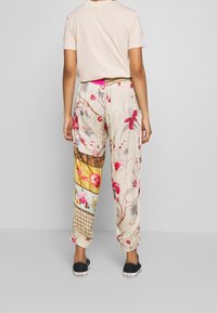 Blommönstrade byxor med elastisk midja och samlade muddarna, med en blandning av färger inklusive beige, röd och gul.