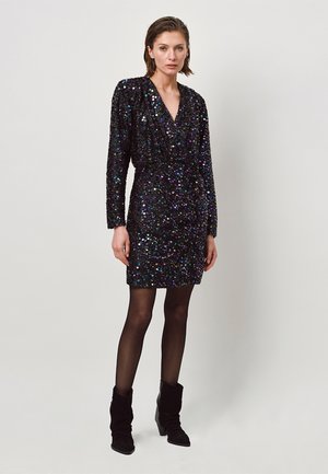 Zwarte paillettenjurk met lange mouwen en een diepe V-hals. Aansluitend silhouet met een geraffineerde taille. Draag met zwarte enkellaarsjes en panty.