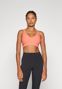 Koral sportsklær med V-hals design, med utskjæringer og teksturert overflate. Kombinert med høy midje svarte tights.