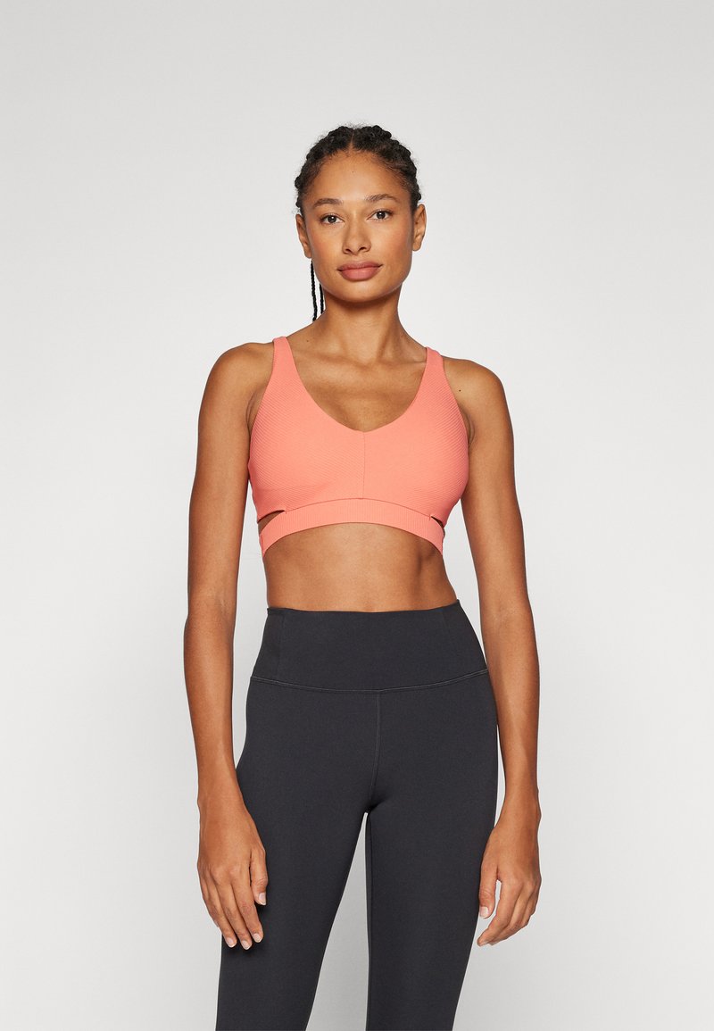 Koral sportsklær med V-hals design, med utskjæringer og teksturert overflate. Kombinert med høy midje svarte tights.