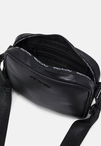 Svart läderaxelväska med ett dragkedjehuvudfack, som har en strukturerad yta och en märkesmärkt, justerbar rem med logodetaljer.