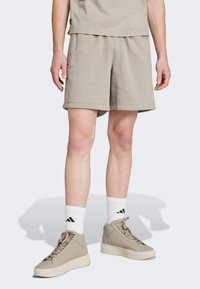 Beige shorts med elastik i taljen, parret med hvide strømper med sort Adidas-logo og beige høj-top sneakers med perforerede detaljer.