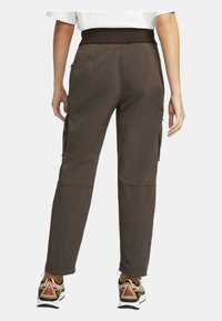 Bruna cargobyxor med en åtsittande midja, sidofickor och avsmalnande ben. Slät textur med en matt yta.