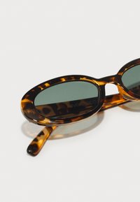 Tortoisekleurige ovale zonnebrillen met donkergroene glazen. Heeft een glanzende afwerking en slanke armen versierd met een luipaardprintpatroon.