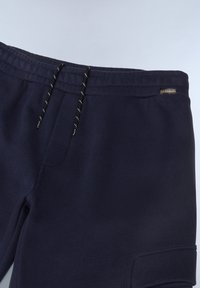 Navy blue sweatpants with a ribbed waistband, drawstrings, and a side pocket, featuring a smooth texture and subtle branding.