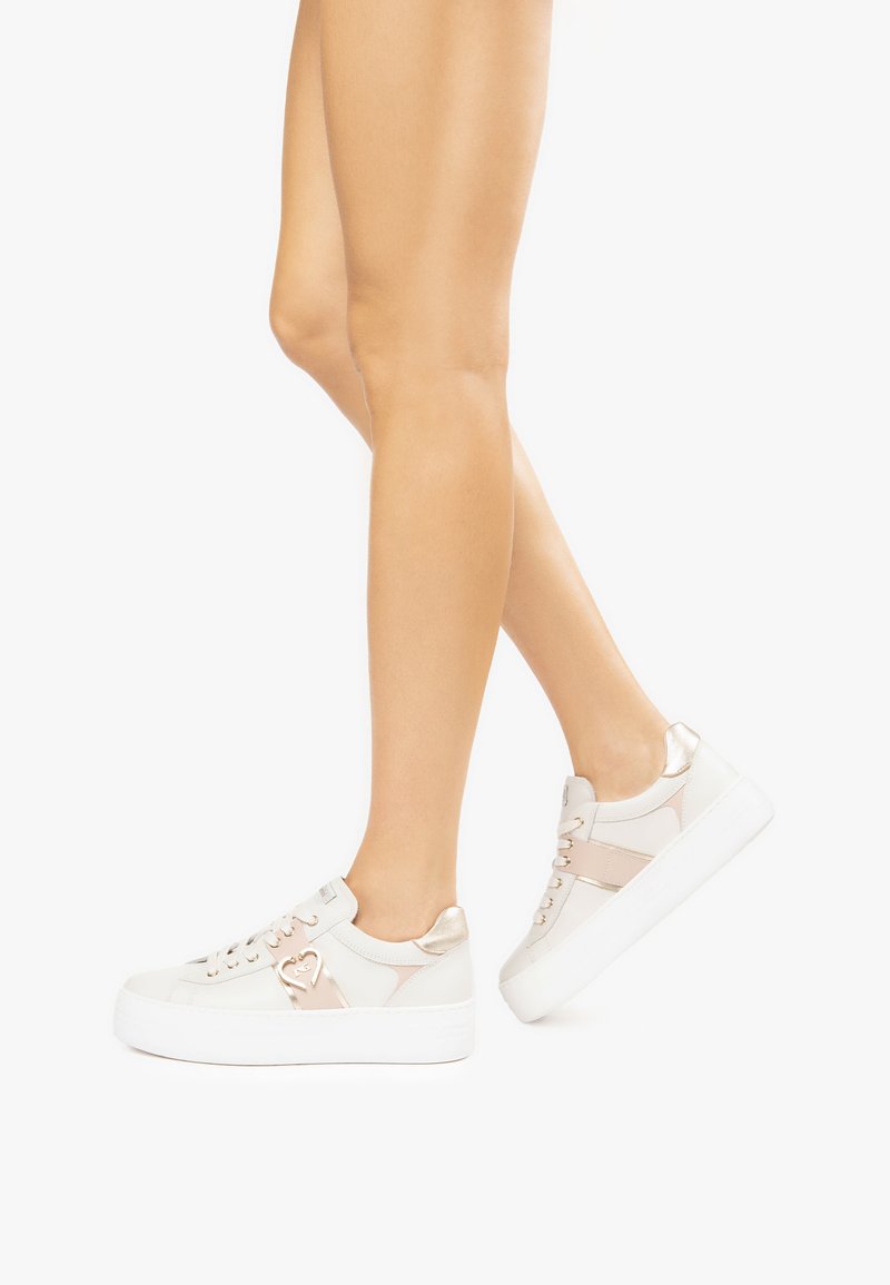 Baskets blanches et beiges avec une finition texturée, comportant des accents métalliques, un logo en forme de cœur et une semelle blanche épaisse. Design minimaliste.